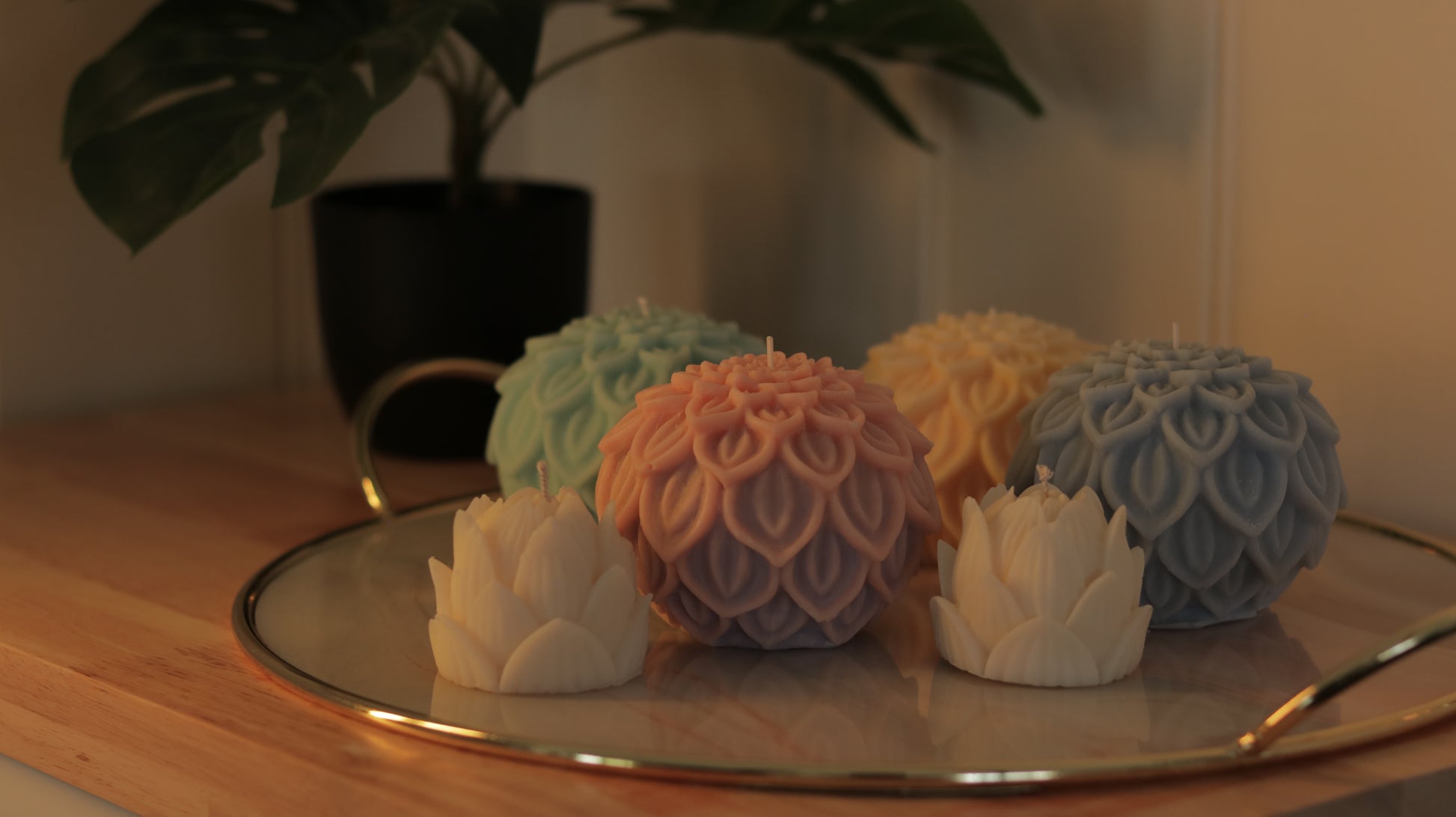 side on image of colourful dahlia and lotus candles arranged artistically on a pink marble and gold tray, not lit.