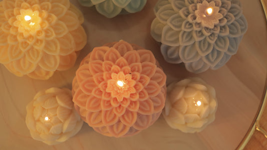 top down image of colourful dahlia and lotus candles arranged artistically and all lit with small flames